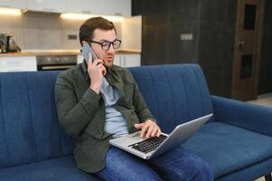 homens trabalhando em computador portátil computador dentro dele sala. casa trabalhos ou estudar, freelance conceito. jovem homem sentado relaxado em sofá com computador portátil. moderno homem de negocios usando computador portátil. foto