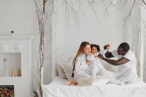 animado multirracial jovem família com pequeno menina criança ter diversão, muito feliz feliz. internacional mãe e Papai jogar com pequeno garota, apreciar final de semana às casa juntos foto