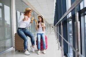 mãe com dela filha às aeroporto terminal com malas comendo velozes Comida foto