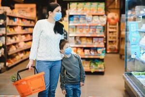 autêntico tiro do mãe e filho vestindo médico máscaras para proteger si mesmos a partir de doença fazer compras para mercearias juntos dentro supermercado foto