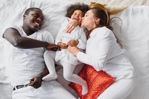 animado multirracial jovem família com pequeno menina criança ter diversão, muito feliz feliz. internacional mãe e Papai jogar com pequeno garota, apreciar final de semana às casa juntos foto