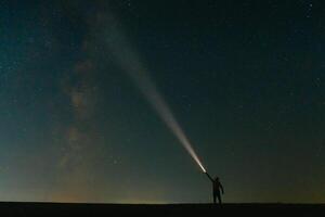 costas Visão do homem com cabeça lanterna em pé em verde gramíneo campo debaixo lindo Sombrio azul verão estrelado céu. noite fotografia, beleza do natureza conceito. Largo panorama, cópia de espaço fundo. foto