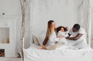 animado multirracial jovem família com pequeno menina criança ter diversão, muito feliz feliz. internacional mãe e Papai jogar com pequeno garota, apreciar final de semana às casa juntos foto