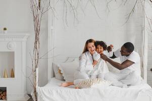 animado multirracial jovem família com pequeno menina criança ter diversão, muito feliz feliz. internacional mãe e Papai jogar com pequeno garota, apreciar final de semana às casa juntos foto