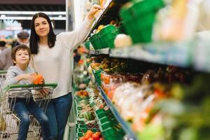 jovem mãe com dela pequeno bebê Garoto às a supermercado. saudável comendo conceito foto