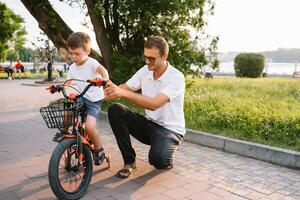 jovem e feliz pai ensina dele jovem filho para passeio uma bicicleta. a criança é feliz . pai assistindo filho. do pai dia. foto