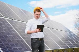 retrato do homem com uma tábua dentro dele mãos em pé perto a solar painéis estação. verde ecológico poder energia geração. solar estação desenvolvimento conceito. casa construção. foto