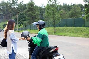 moto Táxi motorista Ojek conectados dando capacete para fêmea cliente foto