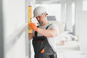 homem segurando nível contra placa de gesso, interior drywall. sótão renovação foto