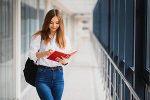 retrato do uma bonita fêmea aluna com livros e uma mochila dentro a universidade corredor foto