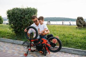 feliz pai e dele filho tendo Diversão juntos às a verde parque, fixação bicicleta junto. do pai dia. foto