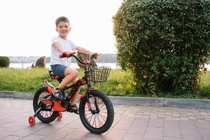 crianças em uma bicicleta às asfalto estrada dentro cedo manhã. pequeno Garoto aprende para passeio uma bicicleta dentro a parque. feliz sorridente criança, equitação uma ciclismo foto