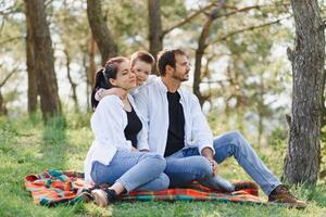 feliz jovem família gastos Tempo ao ar livre em uma verão dia ter Diversão às lindo parque dentro natureza enquanto sentado em a verde grama. feliz família. foto