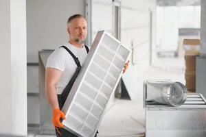uma masculino trabalhador detém a ar filtro para ar condicionamento dentro a escritório espaço. instalação do a ar condicionador. foto