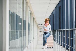 retrato do bem sucedido o negócio mulher viajando com caso às aeroporto. lindo à moda fêmea viagem com bagagem. mulher esperando para avião e bebendo café foto