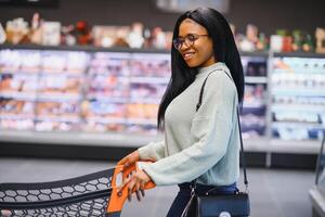 africano americano mulher com compras carrinho carrinho dentro a supermercado loja foto