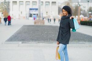 retrato do lindo jovem Preto mulher sorridente com compras bolsas lado de fora foto