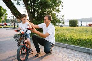 jovem e feliz pai ensina dele jovem filho para passeio uma bicicleta. a criança é feliz . pai assistindo filho. do pai dia. foto