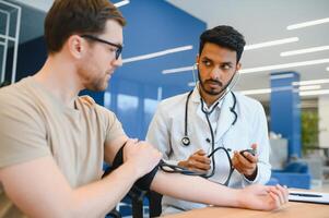 indiano médico segurando discar enquanto medindo do homem sangue pressão foto