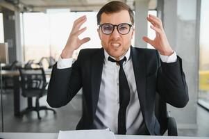 Bravo Senior homem de negocios sentado às dele escrivaninha e gritando foto