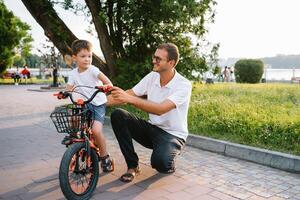 jovem e feliz pai ensina dele jovem filho para passeio uma bicicleta. a criança é feliz . pai assistindo filho. do pai dia. foto