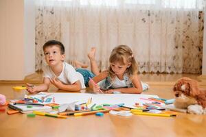 crianças desenhando em chão em papel. pré escola Garoto e menina jogar em chão com educacional brinquedos - blocos, trem, Ferrovia, avião. brinquedos para pré escola e Jardim da infância. crianças às casa ou creche foto