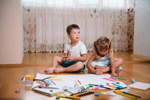 crianças desenhando em chão em papel. pré escola Garoto e menina jogar em chão com educacional brinquedos - blocos, trem, Ferrovia, avião. brinquedos para pré escola e Jardim da infância. crianças às casa ou creche foto