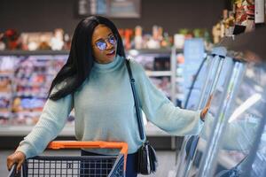 africano americano mulher com compras carrinho carrinho dentro a supermercado loja foto