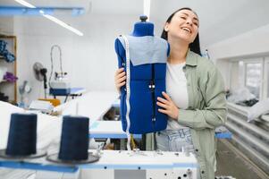 jovem costureira mulher costura roupas em trabalhando mesa. sorridente costureira e dela mão fechar acima dentro oficina. foto