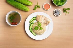 cozido no vapor frango arroz com cru pepino, coentro, salada, molho e sopa servido dentro uma prato isolado em de madeira fundo topo Visão foto