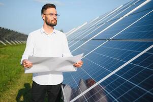 positivo barbudo masculino investidor em pé contra fotovoltaico painéis produzindo alternativo energia. foto