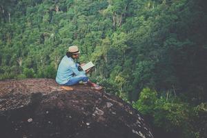 homem asiático viajar relaxar no feriado. assentos relaxem, leiam livros em penhascos rochosos. na montanha. Na Tailândia foto