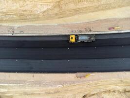 amarelo caminhão derramando betume sobre uma Novo estrada. aéreo zangão tomada. estrada construção dentro progresso em declive natureza canyon. a infraestrutura desenvolvimento e logística. foto