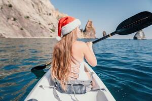 mulher dentro caiaque costas visualizar. feliz jovem mulher dentro santa chapéu flutuando dentro caiaque em calma mar. verão feriado período de férias e alegre fêmea pessoas relaxante tendo Diversão em a barco. foto