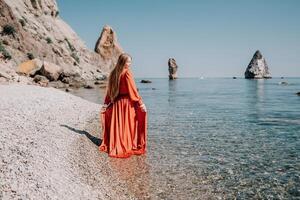 mulher viagem mar. feliz turista dentro vermelho vestir apreciar levando cenário ao ar livre para recordações. mulher viajante posando em a Rocha às mar baía cercado de vulcânico montanhas, partilha viagem aventura viagem foto