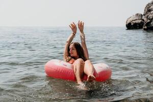 mulher verão mar. feliz mulher natação com inflável rosquinha em a de praia dentro verão ensolarado dia, cercado de vulcânico montanhas. verão período de férias conceito. foto