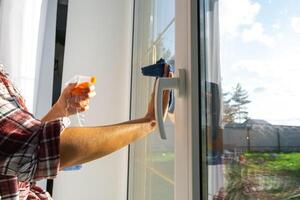 mulher manualmente lavagens a janela do a casa com uma trapo com spray limpador e esfregão dentro a interior com branco cortinas. restaurando ordem e limpeza dentro a primavera, limpeza servise foto