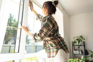 mulher manualmente lavagens a janela do a casa com uma trapo com spray limpador e esfregão dentro a interior com branco cortinas. restaurando ordem e limpeza dentro a primavera, limpeza servise foto