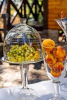 mesa decoração com vidro e cristal talheres. uvas debaixo cúpula cobrir e pêssegos dentro vaso. fechar-se. foto