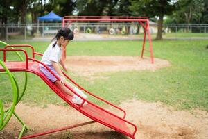 sorriso de linda garota asiática brinca na escola ou jardim de infância ou playground. atividade de verão saudável para crianças. menina asiática escalando ao ar livre no playground. criança brincando no playground ao ar livre. foto