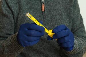 amarelo fita a medida dentro masculino mãos dentro azul luvas. foto