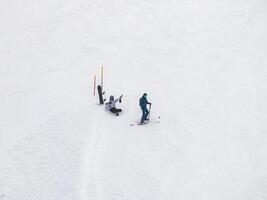 três esquiadores, com 1 caído, em a zermatt recorrer encostas, suíço Alpes. foto