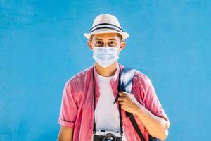 latim americano homem viajante com vintage Câmera e segurando uma mochila vestindo uma protetora mascarar. foto