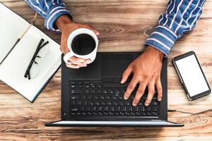 mãos do uma homem segurando uma copo do café e digitando em uma computador portátil, escritório trabalhos conceito. Eu trabalhos on-line. foto