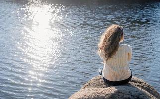 mulher romântica e atenciosa sentada na margem do rio ao pôr do sol no dia de outono foto