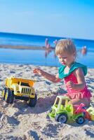 feliz criança pequena criança jogando em a de praia com brinquedo carro.verão período de férias viagem conceito. vertical foto. foto