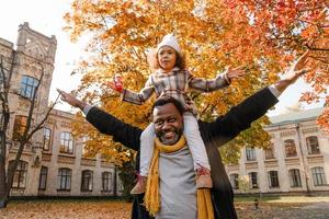 garota negra se divertindo e sentada no pescoço de seu avô no parque outono