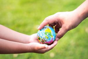 unindo forças para cuidar do global. fundo gramado verde turva. proteja nosso globo. as mãos de uma mãe passam um pequeno mundo para as mãozinhas de seu bebê. para ajudar a proteger e manter nosso planeta habitável.