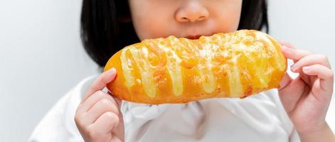 menina asiática comendo torradas doces. criança feliz segurando lindo coque longo nas mãos.