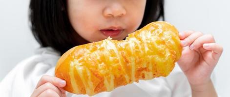 linda criança segura um delicioso pão comprido na frente do rosto, preparando-se para comê-lo com gosto. lanches que as crianças gostam. foto